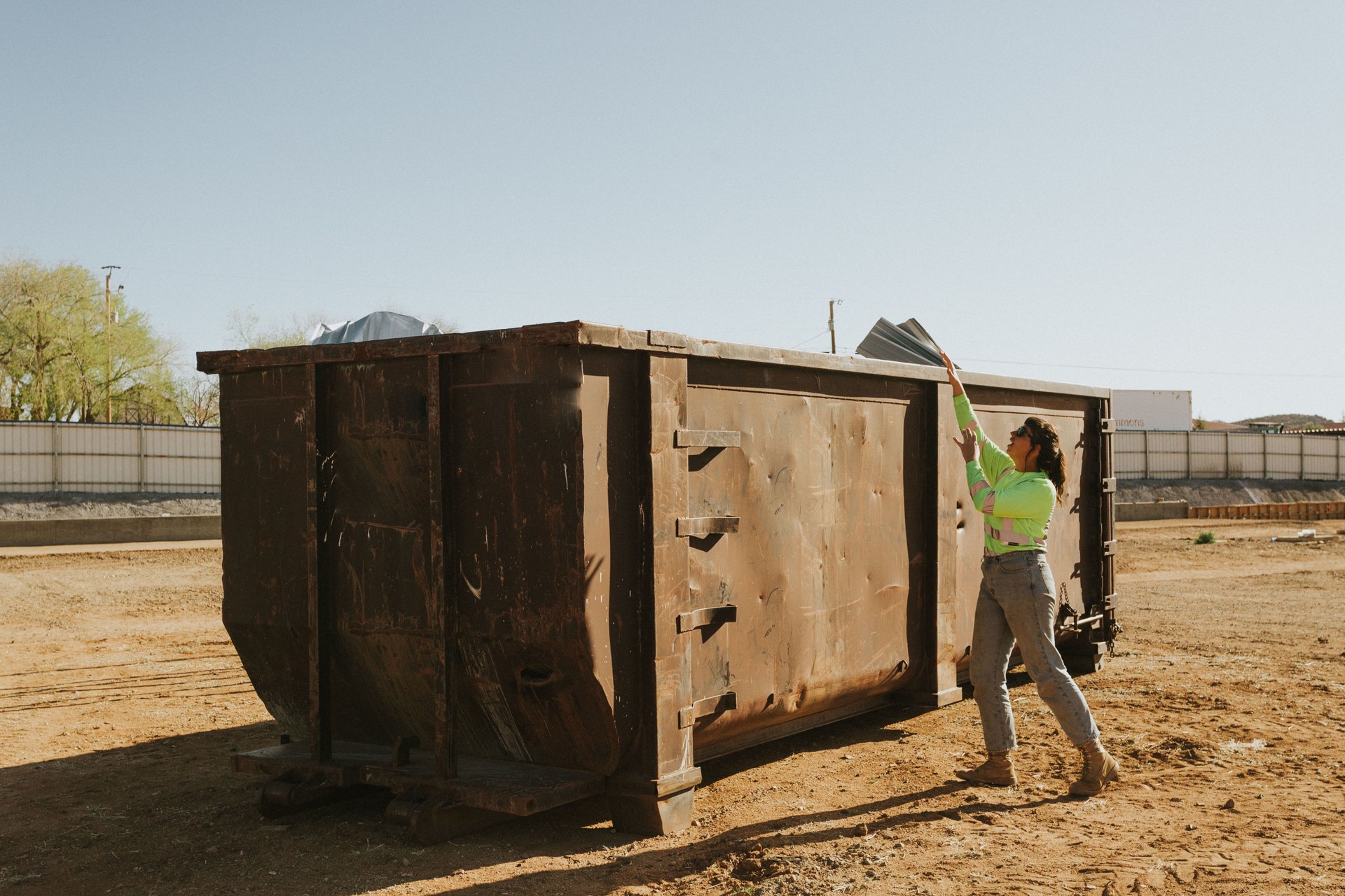 Construction woman throwing items in giant dumpster